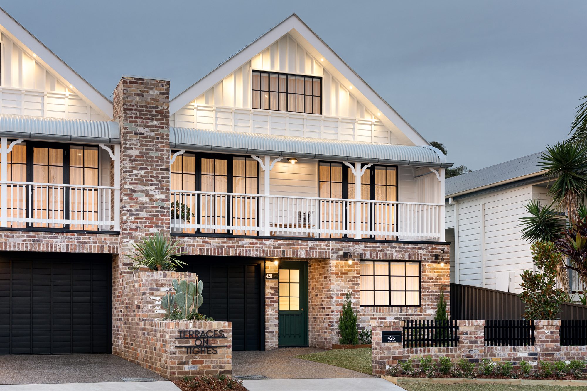 Terraces on Tighes, Tighes Hill — dusk front facade with recycled brick, gabled roof and warm interior glow